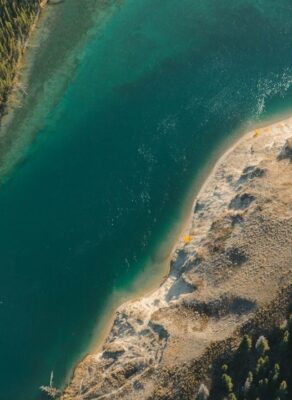 Luchtfoto van een diepblauw meer met beboste en zandige oevers