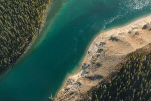 Luchtfoto van een diepblauw meer met beboste en zandige oevers