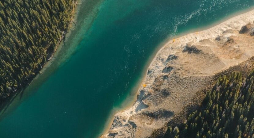 Luchtfoto van een diepblauw meer met beboste en zandige oevers